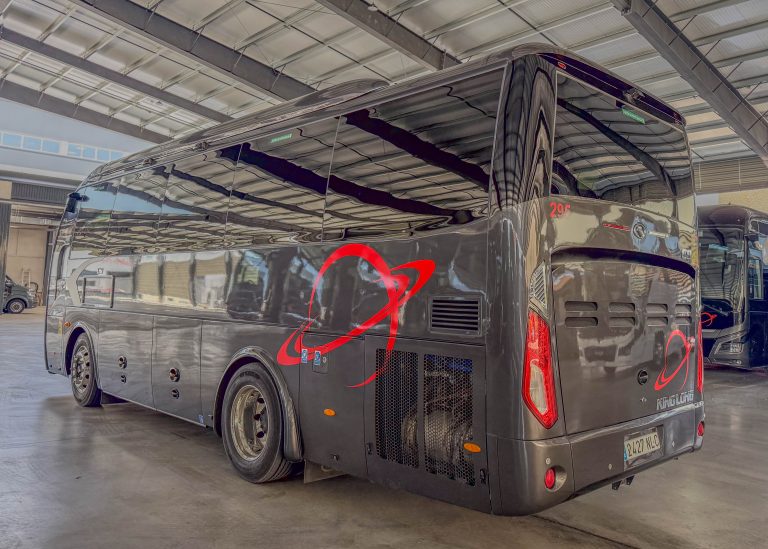 Black luxury coach bus parked indoors, showing the rear and side with red decorative graphics in a maintenance hangar.