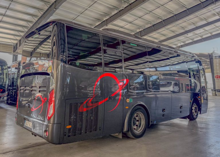 Black luxury coach inside a bright indoor showroom, featuring red decorative swooshes along the glossy side and large windows.”] ,