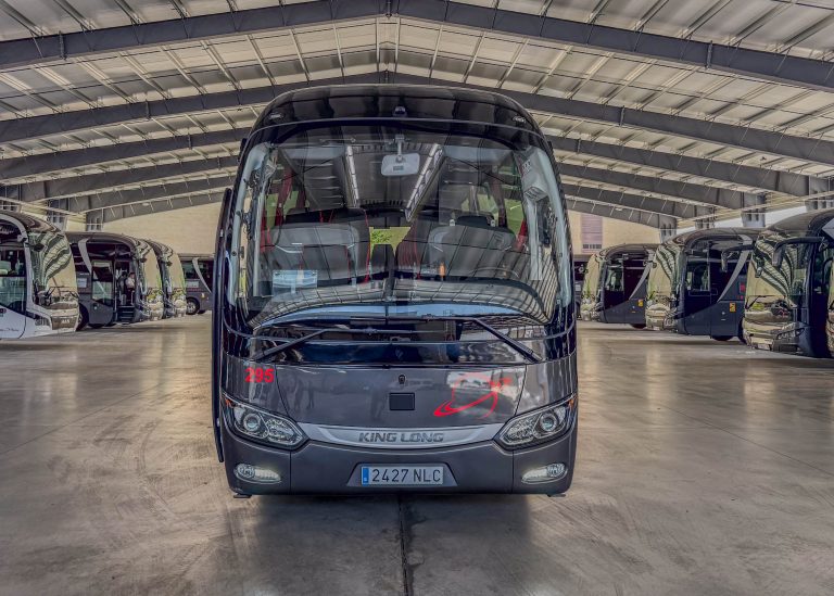 Front view of a black King Long bus inside a large indoor bus depot, with other buses lined up on both sides of the aisle.