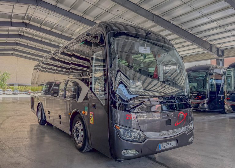 Front-angle view of a sleek black King Long coach on display in an indoor showroom with a metal-framed roof; reflections on the glossy exterior.