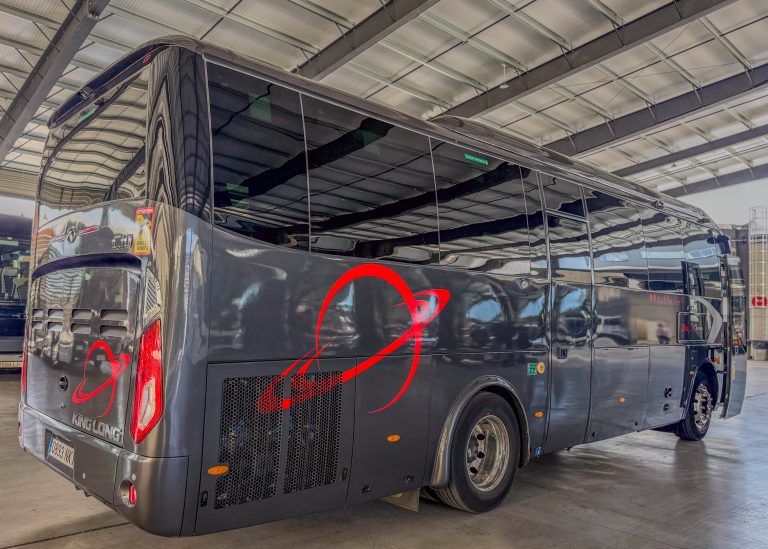 Black luxury coach bus parked inside a large indoor maintenance hangar, showing a red decorative swirl on its side.