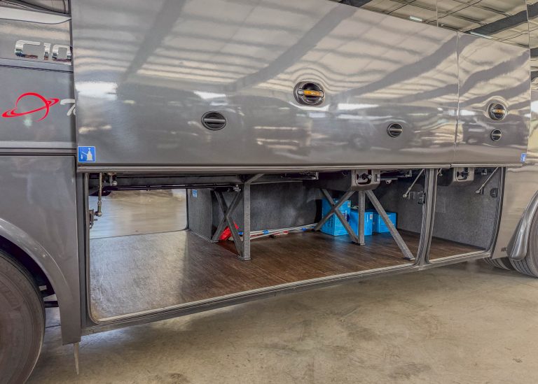 Open side storage compartment of a gray truck, showing metal support structure and tools inside when the door is lifted