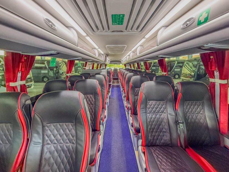 Front-to-back view of a bus interior, rows of black seats with red piping along the aisle and red curtains on both sides.